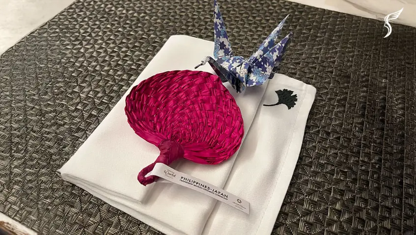 Decorative setup with a red woven fan and origami crane atop a folded napkin for the Philippines-Japan celebration.