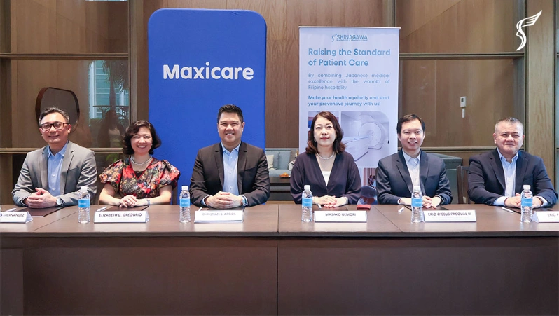 Executives from Shinagawa Diagnostic & Preventive Care and Maxicare sit together during a partnership event, with branding banners and nameplates displayed in front.