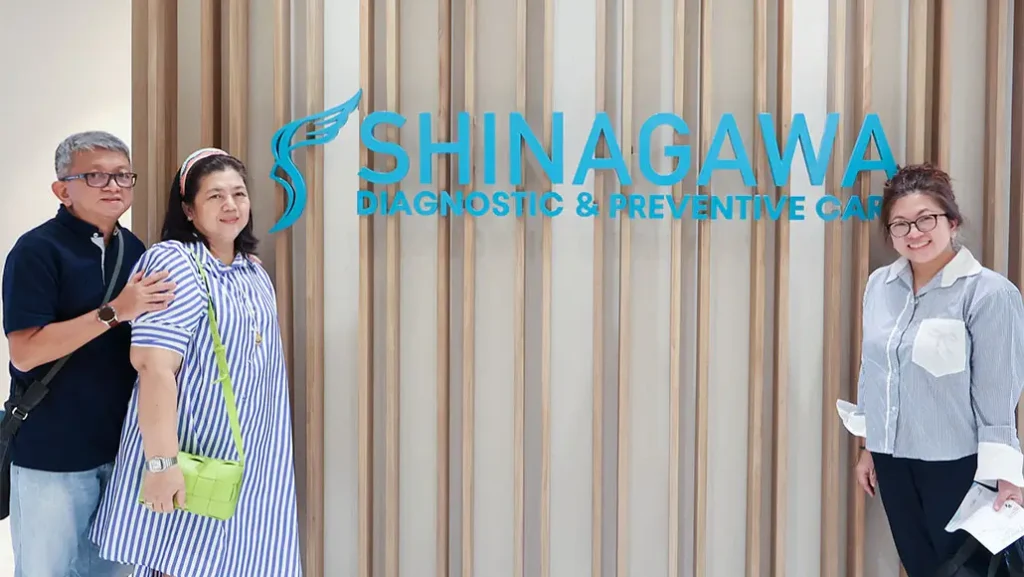 visitors pose for a photo with a smiling Shinagawa staff member in front of the Shinagawa Diagnostic & Preventive Care sign.