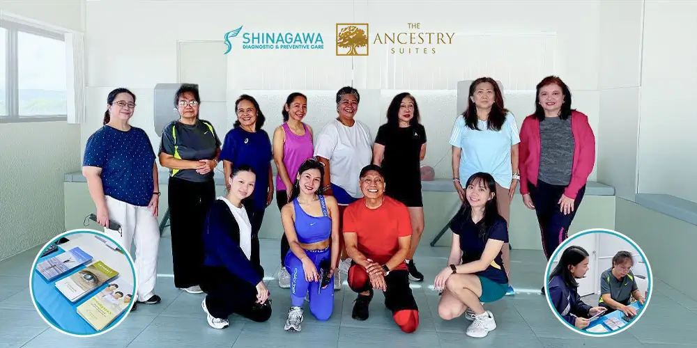 Group photo of fitness class participants in activewear smiling after a workout session inside a well-lit indoor studio with beige walls and large windows.