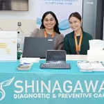 Shinagawa Diagnostic & Preventive Care representatives at an indoor health booth offering random blood sugar testing and wellness brochures at a corporate event.