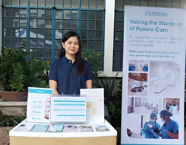 Shinagawa Diagnostic & Preventive Care representative at an outdoor booth displaying healthcare brochures and a banner promoting advanced preventive medical services.
