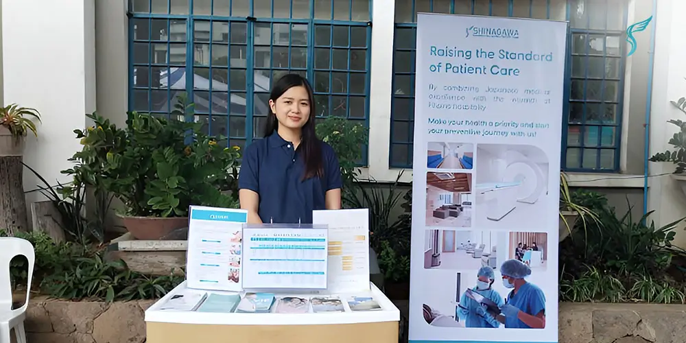 Shinagawa Diagnostic & Preventive Care representative at an outdoor booth displaying healthcare brochures and a banner promoting advanced preventive medical services.