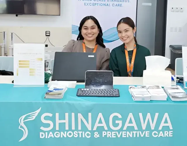 Shinagawa Diagnostic & Preventive Care representatives at an indoor health booth offering random blood sugar testing and wellness brochures at a corporate event.