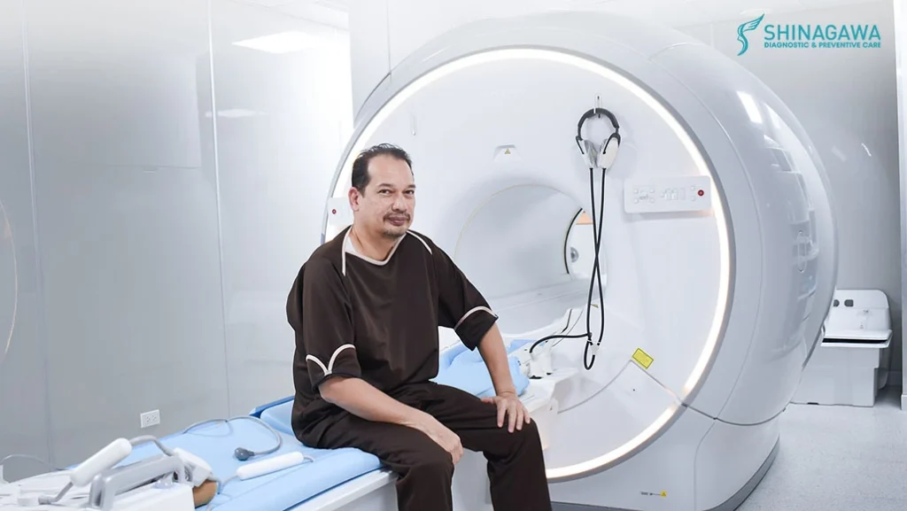 Male patient seated beside an MRI machine at Shinagawa Diagnostic & Preventive Care, preparing for a diagnostic imaging procedure in a modern medical facility.