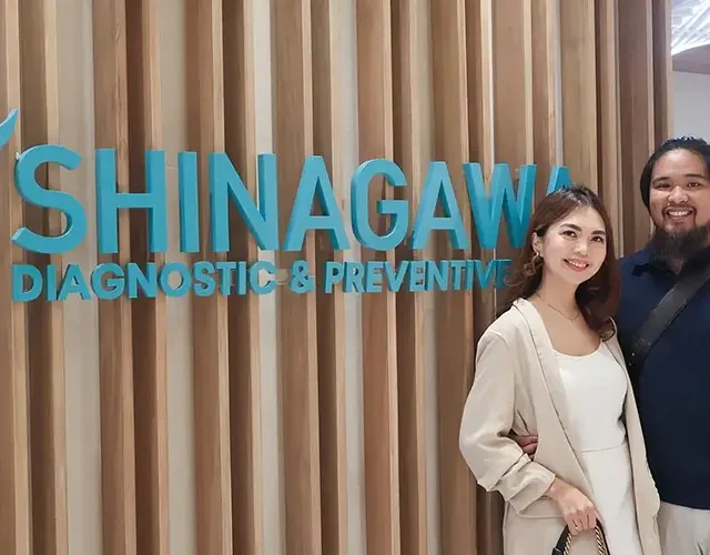 Happy couple posing in front of the Shinagawa Diagnostic & Preventive Care logo wall, reflecting a positive healthcare experience at the clinic.