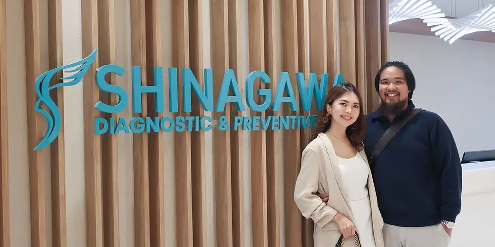 Happy couple posing in front of the Shinagawa Diagnostic & Preventive Care logo wall, reflecting a positive healthcare experience at the clinic.